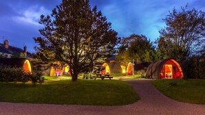 A rustic campsite with several wooden cabins, a picnic table, and a large tree in the center. - Podumna Village  (Portumna)