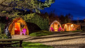 Two dome-shaped cabins with interior lighting, a picnic table, and a statue in the foreground. - Podumna Village  (Portumna)