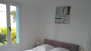 A bedroom with a bed, nightstands, a window, and a wall-mounted artwork. - Gîte "des Flots" Proche mer (Saint-Michel-en-l'Herm)
