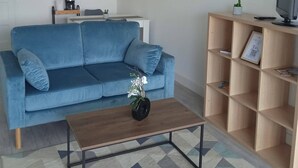A living room with a blue sofa, a wooden coffee table, a bookshelf, and a television. - Gîte "des Flots" Proche mer (Saint-Michel-en-l'Herm)