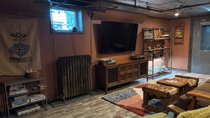 Ein gemütliches Wohnzimmer mit einem großen Flachbildfernseher, Holzmöbeln, einer Heizung und einem Fenster mit Blick.