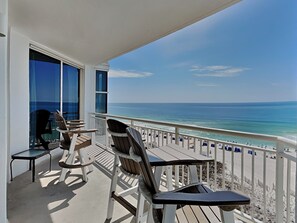 A balcony with a view of the ocean, wooden chairs, and a table.