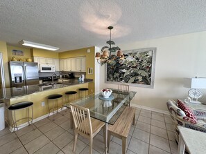 Enjoy meals at the kitchen table with seating for three, surrounded by a vibrant tropical-themed painting.