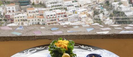 A table with food and a book, overlooking a coastal town with buildings on a hillside.