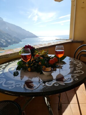 A table with two glasses of red wine, a bowl of snacks, and a fruit arrangement on a balcony overlooking a coastal view. - La vedetta Sea View (Positano)