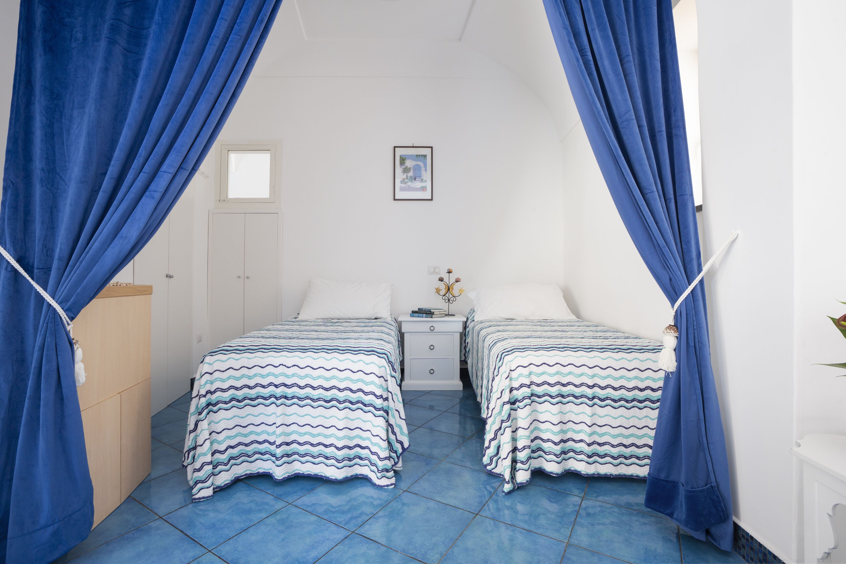 A room with two beds, a nightstand, a dresser, and blue curtains.