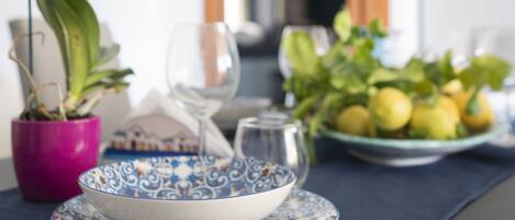 A dining table set with a blue and white patterned bowl, a pink vase with white flowers, and a plate of lemons.