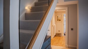 Een trap met beklede treden en een houten leuning, die leidt naar een ruimte met een deur en een radiator.