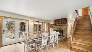 Un comedor con una mesa y sillas de madera, una chimenea y una escalera de madera.