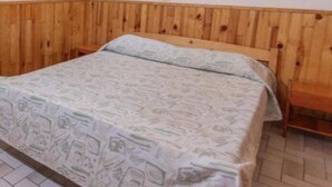 A single bed with a patterned bedspread in a room with wooden paneling on the walls and a tiled floor. - Gite 3 Personnes (Ambrugeat)
