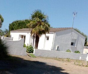 Une maison de plain-pied avec une façade blanche et un toit brun.