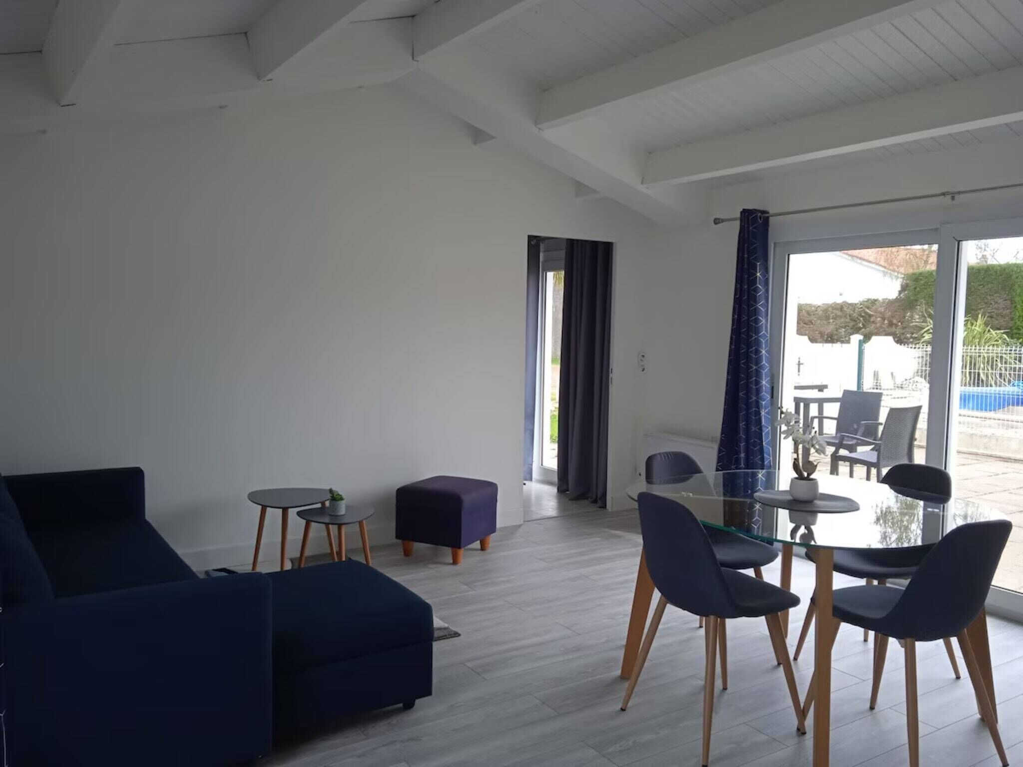 A modern living room with a dark blue sofa, a glass dining table with chairs, and a small side table with a plant.