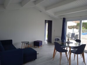 Un salon moderne avec un canapé bleu foncé, une table à manger en verre entourée de chaises et une petite table d’appoint agrémentée d’une plante.
