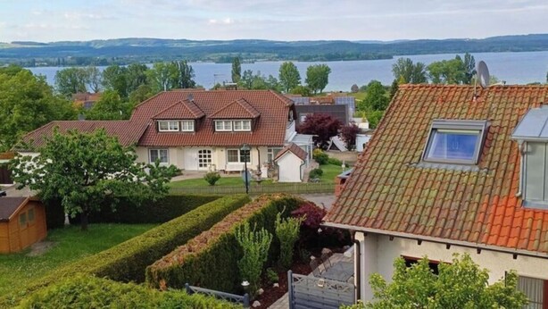 A residential area with houses, a well-maintained garden, and a lake in the background. - Ferienwohnung auf der Höri, Terrasse und Garten, 8 Minuten Fußweg zum Bodensee (Gaienhofen)