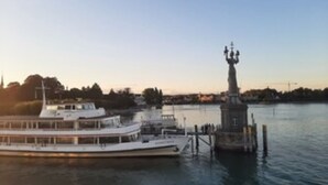 A riverfront with a large white boat docked at a pier, a statue, and buildings in the background. - Ferienwohnung auf der Höri, Terrasse und Garten, 8 Minuten Fußweg zum Bodensee (Gaienhofen)