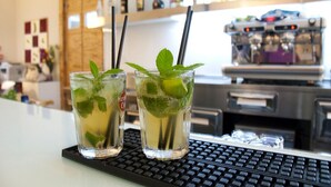 Two glasses of a beverage with mint leaves on a bar counter, with a coffee machine and various bottles in the background.