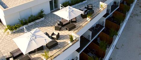 A multi-story hotel with outdoor seating areas, including sofas and umbrellas, overlooking a beach.