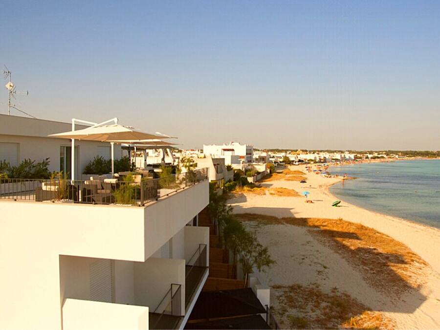 Hotel amb terrasses davant del mar, platja de sorra i cel blau.