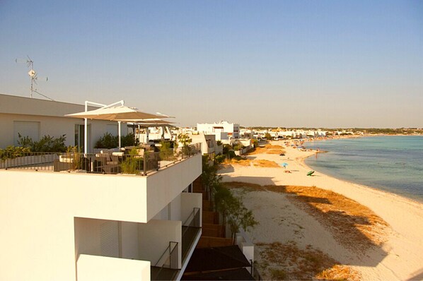 Hotel frente al mar con balcones que dan al océano, una playa de arena y cielo despejado.