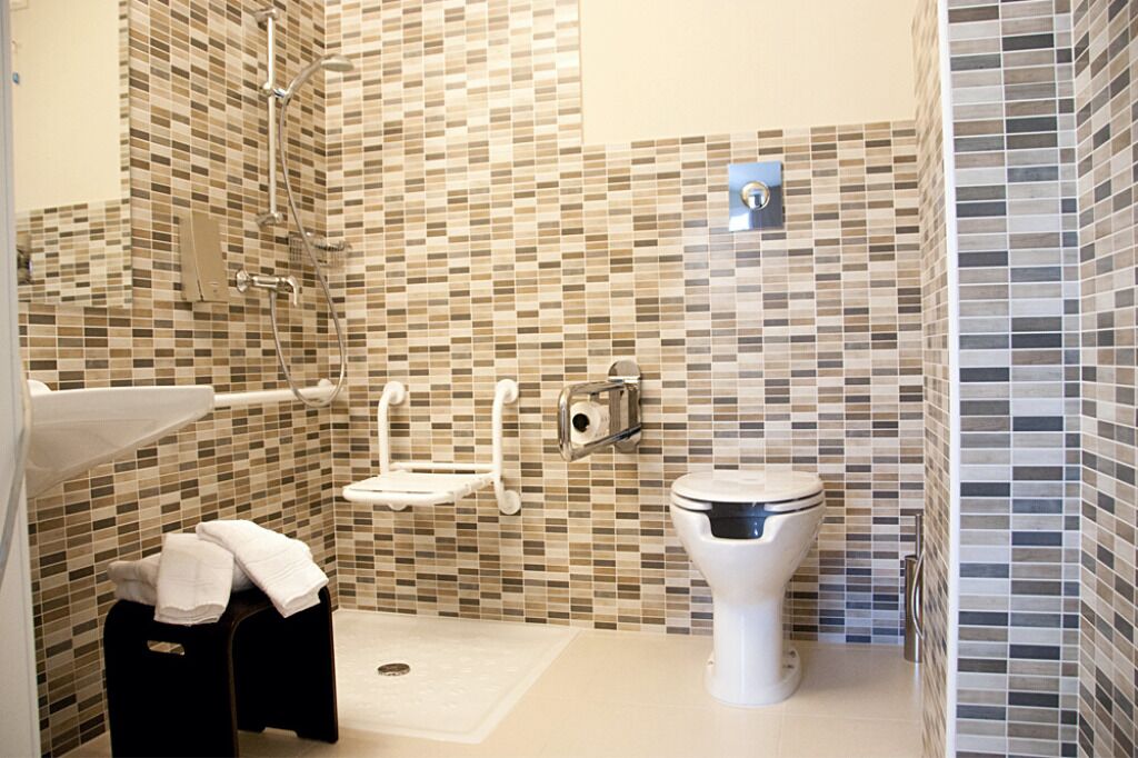 Une salle de bain avec un mur recouvert de mosaïques, des toilettes, un lavabo et un espace douche.