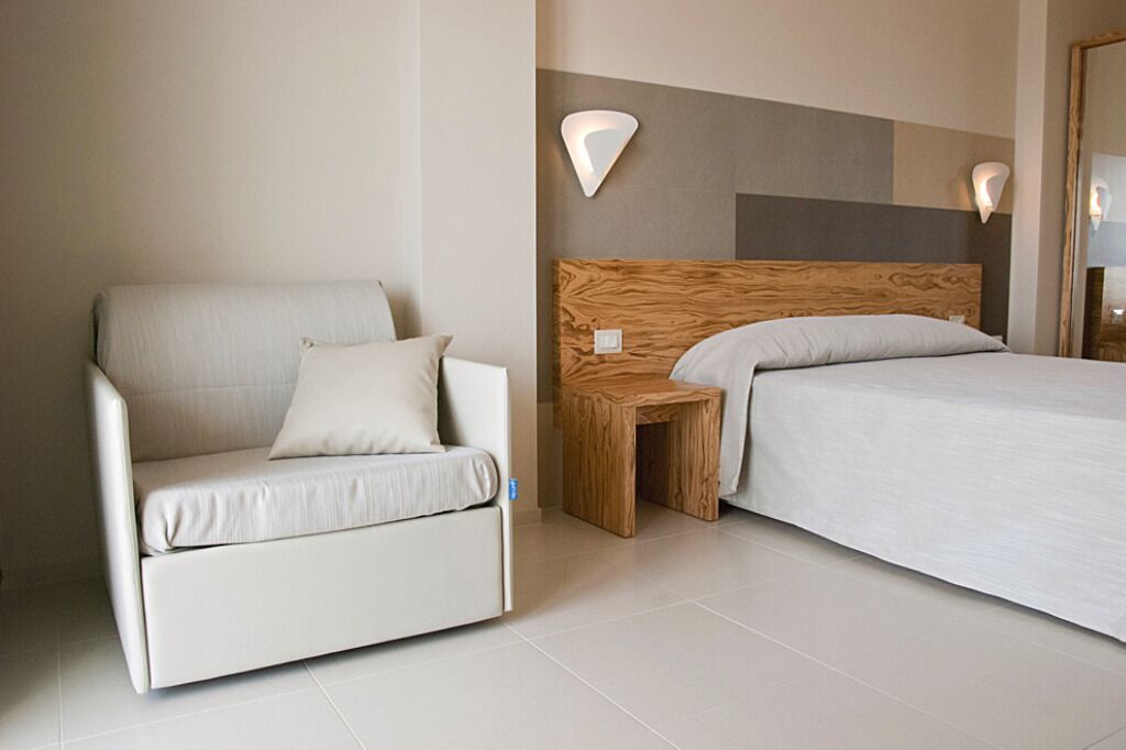 A modern hotel room with a sofa, a wooden nightstand, and a bed.