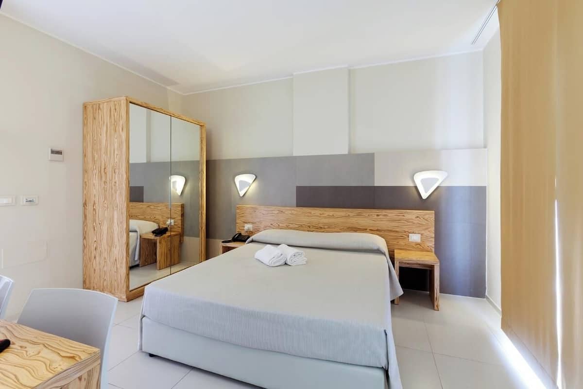 Een moderne hotelkamer met een groot bed, een houten garderobe, een nachtkastje en een stoel.