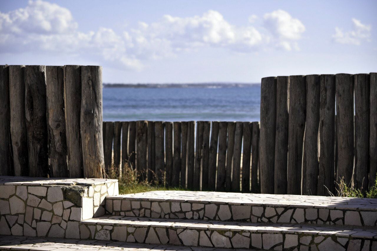 Una valla de madera con una escalera de piedra que lleva a una plataforma de observación con vista al océano.