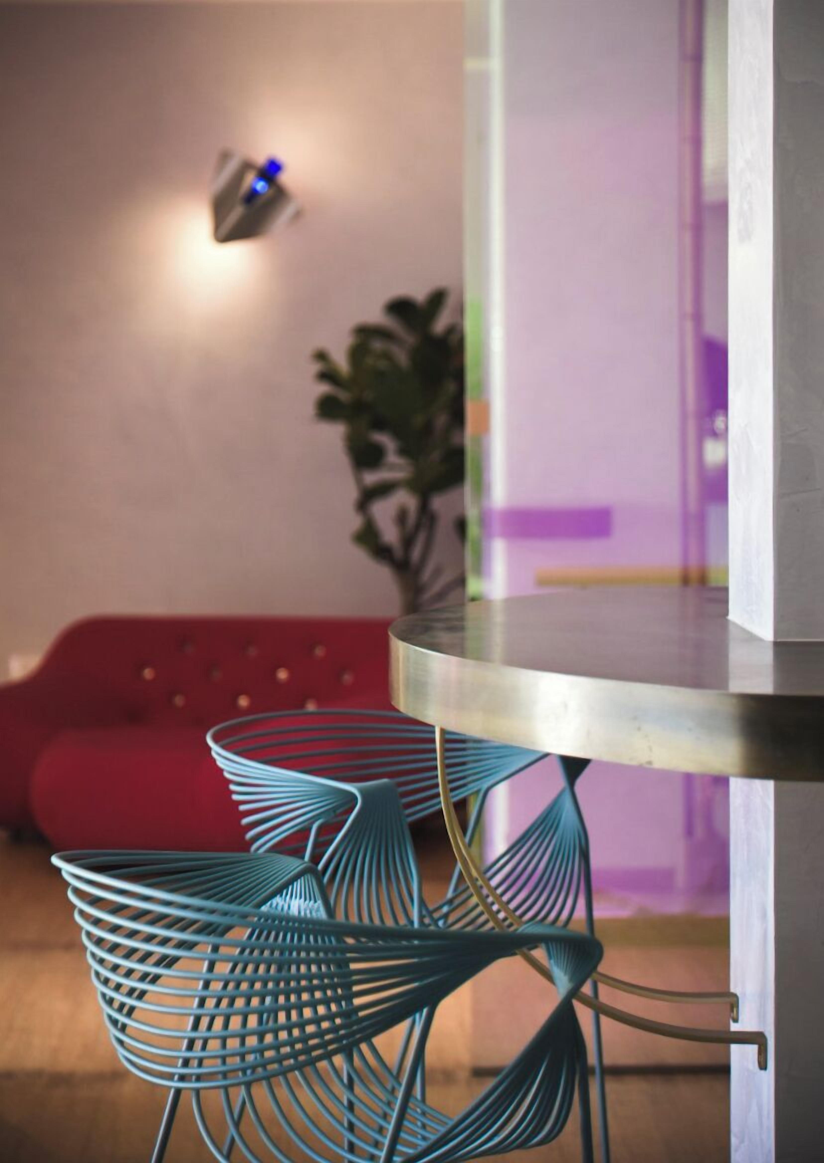 Een modern interieur met een ronde metalen tafel, teal draadstoelen, een rode bank en een wandlamp.