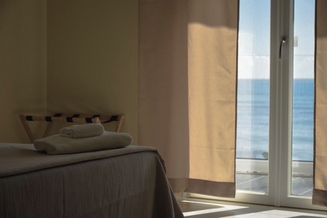 Camera d'albergo con un letto, vista sul mare tramite una porta scorrevole e una finestra con tende.