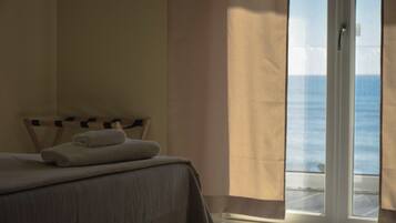 Camera d'albergo con un letto, vista sul mare tramite una porta scorrevole e una finestra con tende.