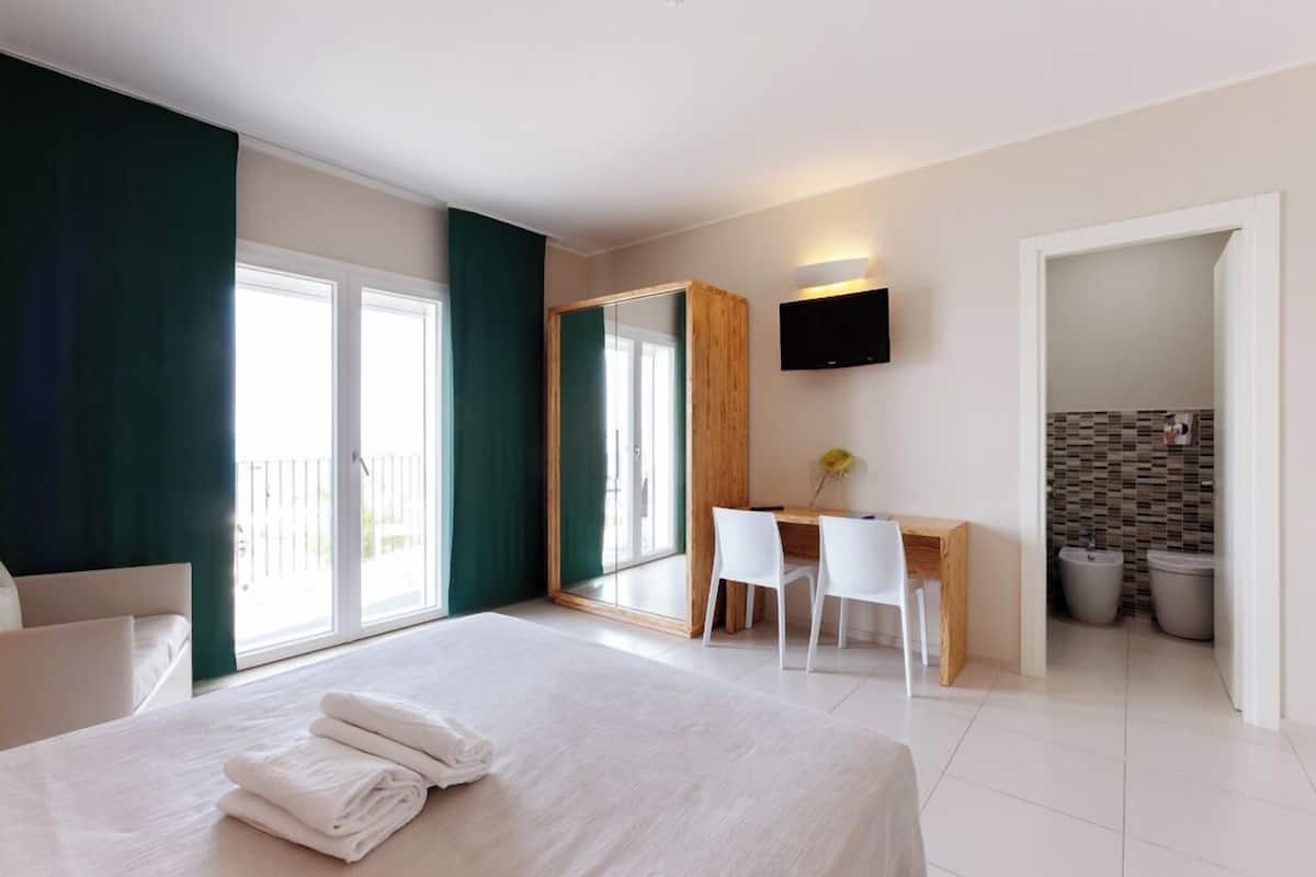 Een hotelkamer met een bed, een bureau, twee stoelen, een televisie en een badkamer die door een open deur zichtbaar is.