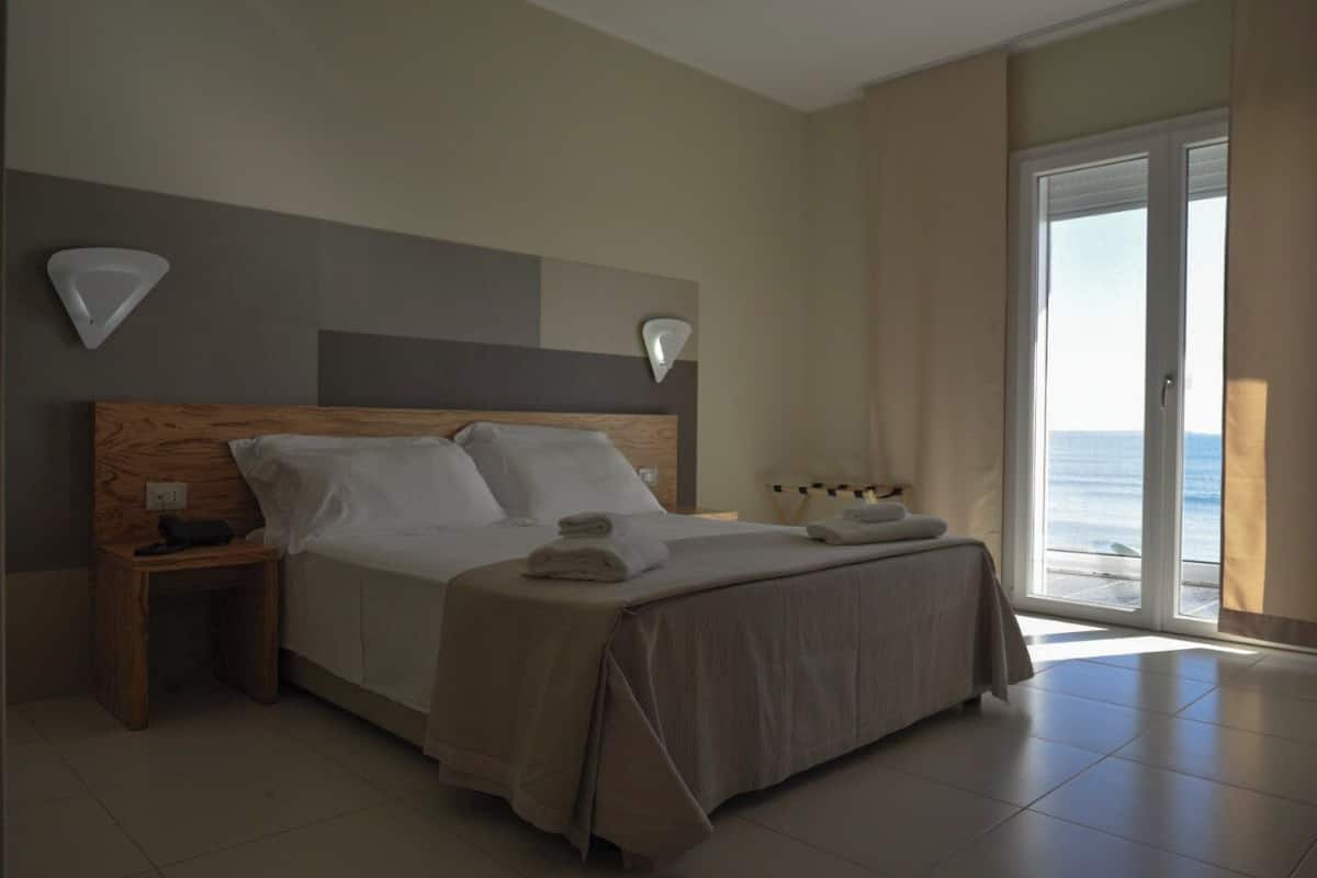 Een slaapkamer met een groot bed, nachtkastjes en uitzicht op zee door een schuifdeur.