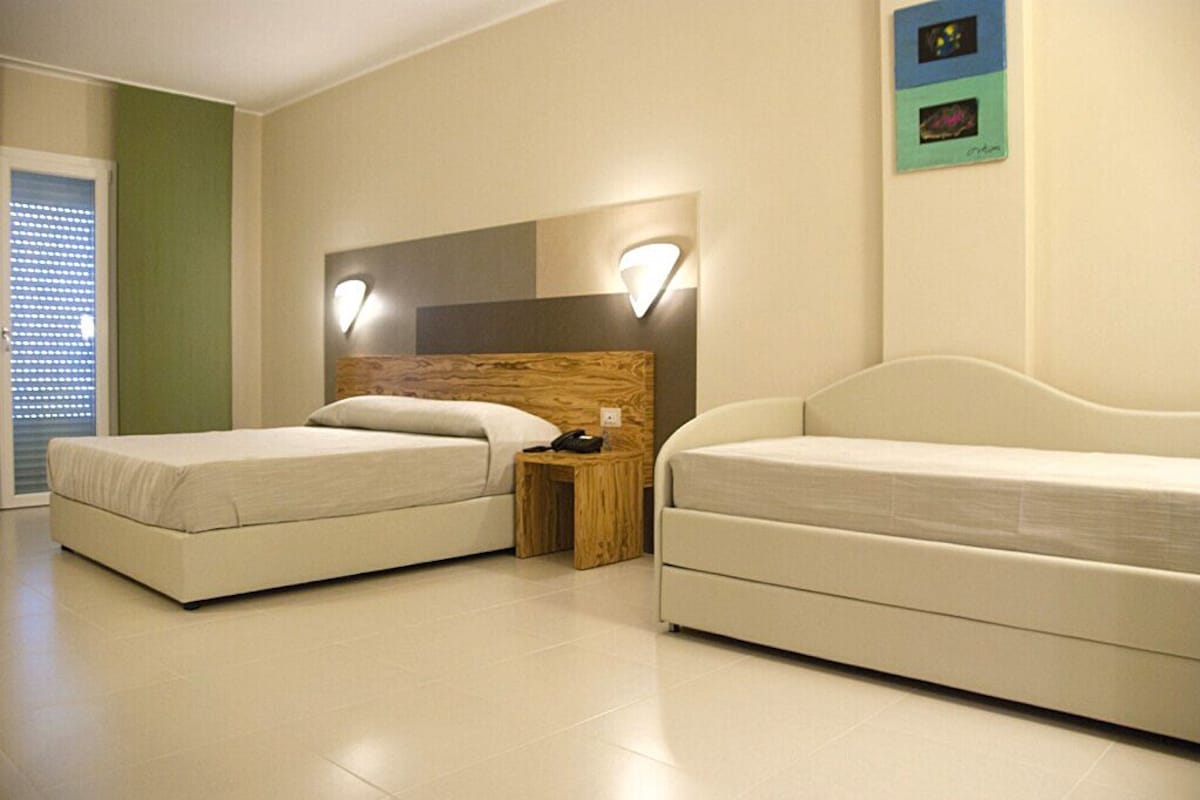 A hotel room with two beds, a wooden headboard, a bedside table, and a wall-mounted light fixture.