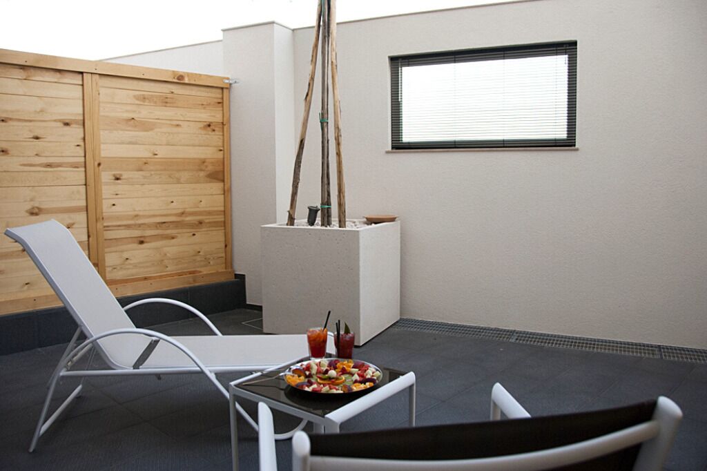 Un patio con una mesa blanca, dos sillas blancas, una cerca de madera y una ventana con persianas.