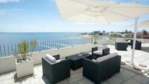 An outdoor patio with wicker furniture, a large umbrella, and a view of the sea.