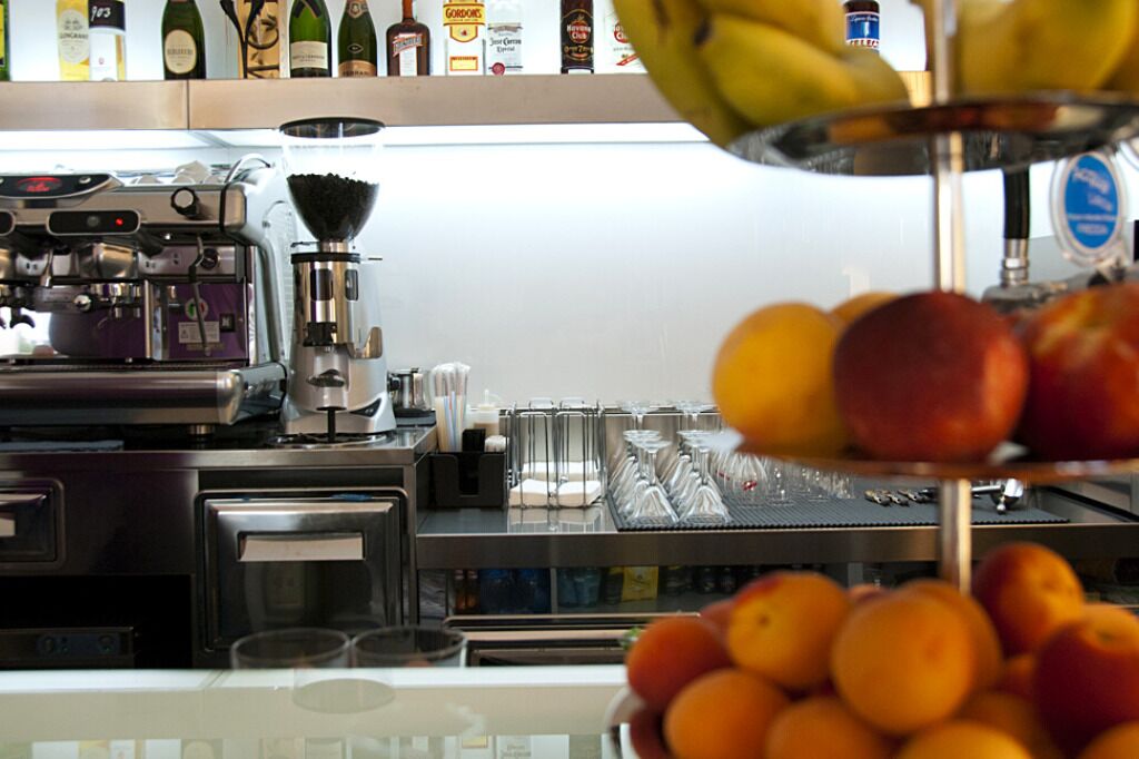 A bar area with a coffee machine, a fruit display, and a shelf with bottles.
