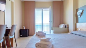 A hotel room with a bed, a desk, chairs, a small table, and a view of the balcony.