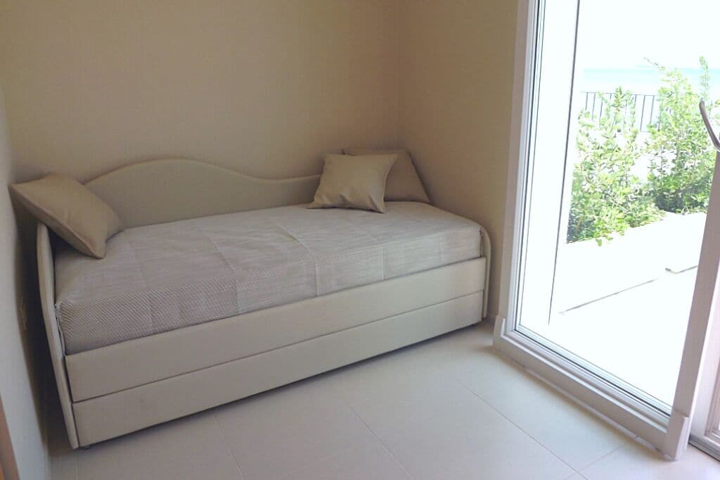 A single bed with a headboard and two pillows in a room with a large window.