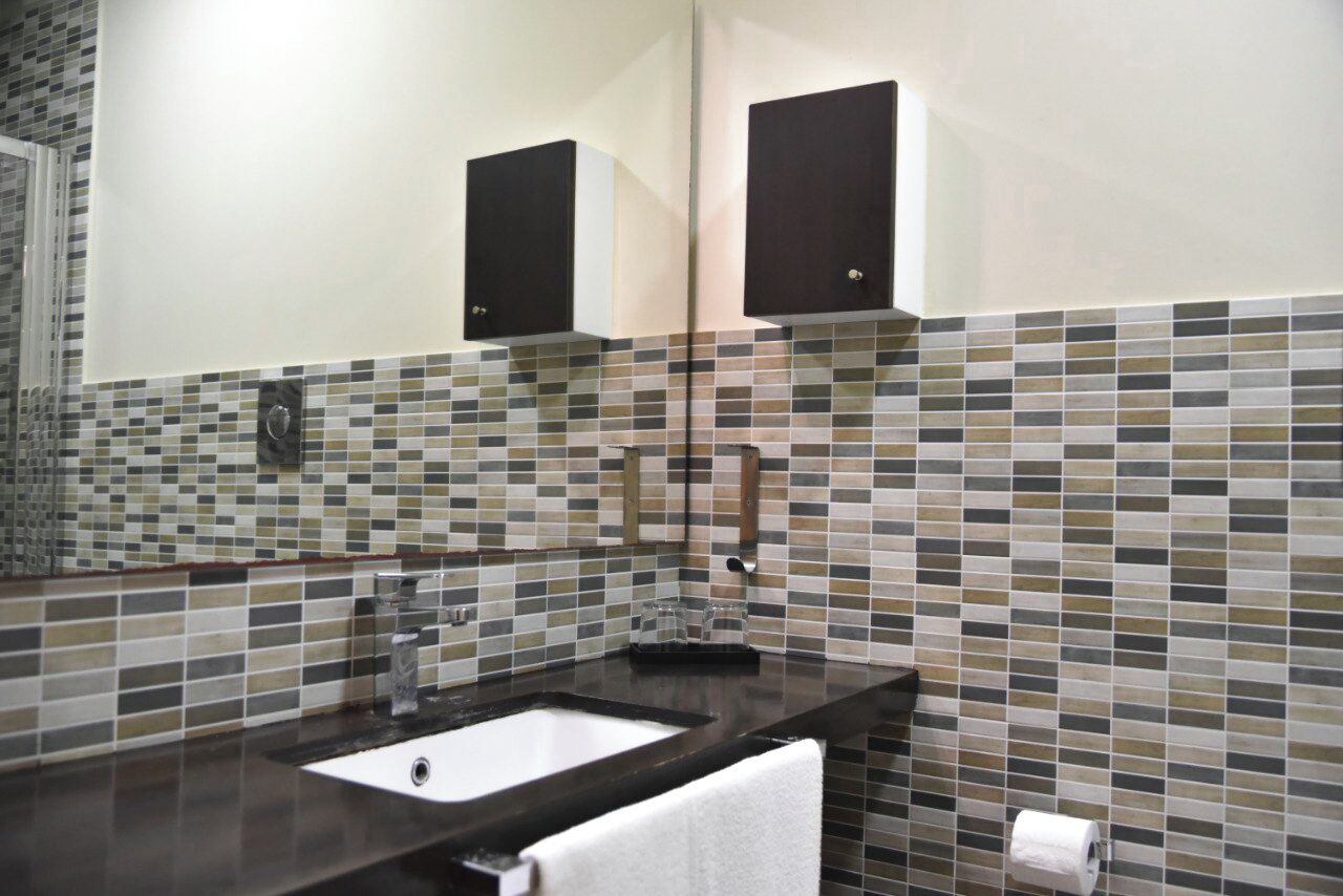 A bathroom with a tiled backsplash, a sink, a mirror, and two cabinets.