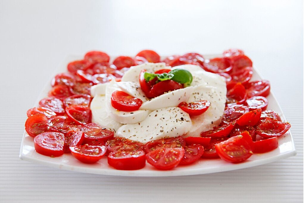 Ein Teller mit Caprese-Salat, Mozzarella, Tomaten und Basilikum.