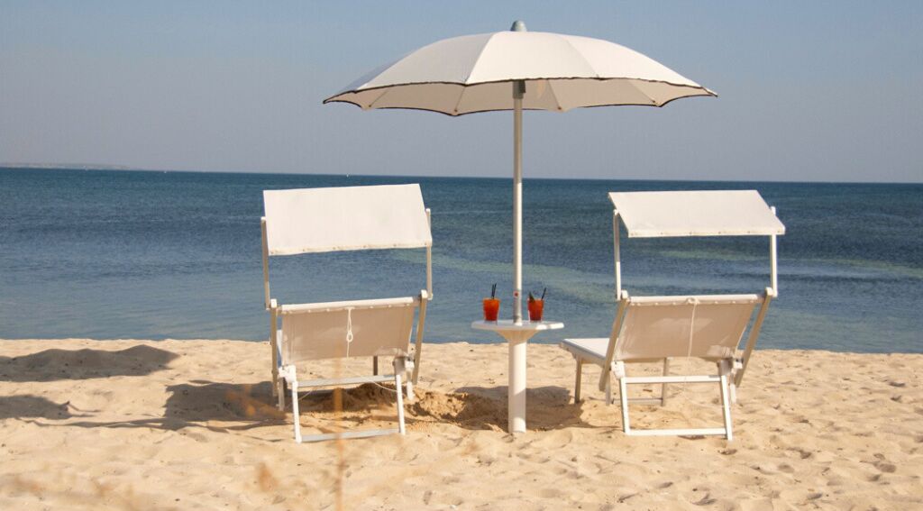 Due sedie da spiaggia con tende parasole bianche e un tavolino con bevande, con vista sulla spiaggia sabbiosa e sull'oceano.
