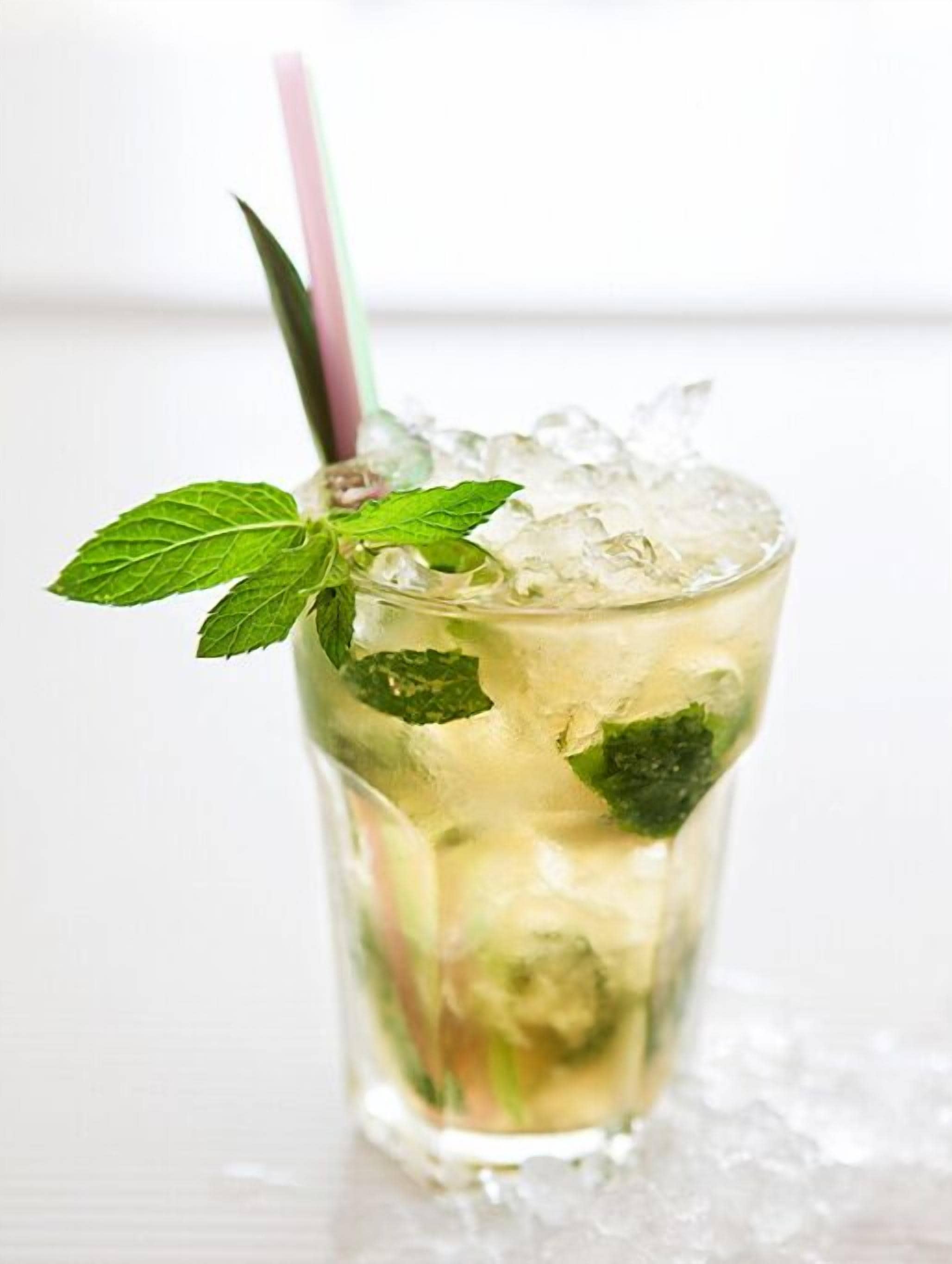 Un vaso alto con pajita rosa, lleno de un líquido transparente, cubitos de hielo y hojas de menta verdes.