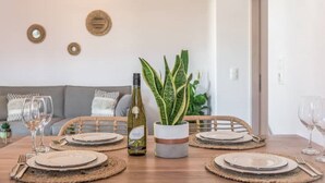 A dining table set with plates, cutlery, and a bottle of wine, with a plant in a pot and a sofa in the background. - Esperanza Apartment (Adamantas)