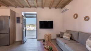 A modern living room with a sofa, a flat-screen TV, and a wooden ceiling. - Esperanza Apartment (Adamantas)