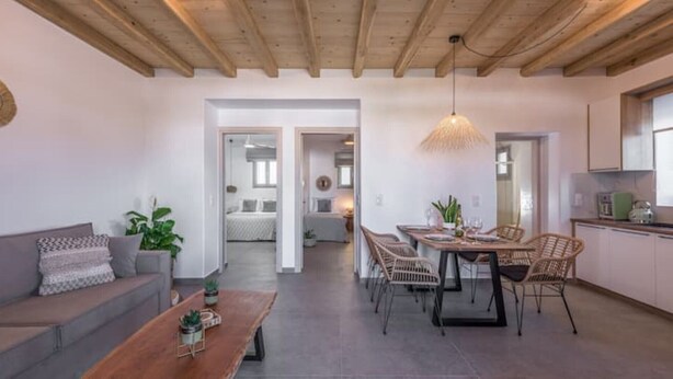 A modern living room with a wooden ceiling, a dining area with a table and chairs, and a kitchen area with cabinets and appliances. - Esperanza Apartment (Adamantas)