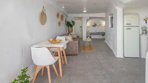 A modern kitchen with a white refrigerator, a dining area with a white table and chairs, and a living area with a sofa and a coffee machine. - Esperanza Boathouse (Mandrakia)