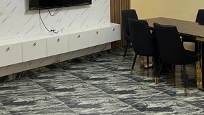 A modern dining area with a marble-patterned wall, a flat-screen TV mounted above a white console, and a dining table with black chairs. - Blue Icon Apartment  (Loburo)