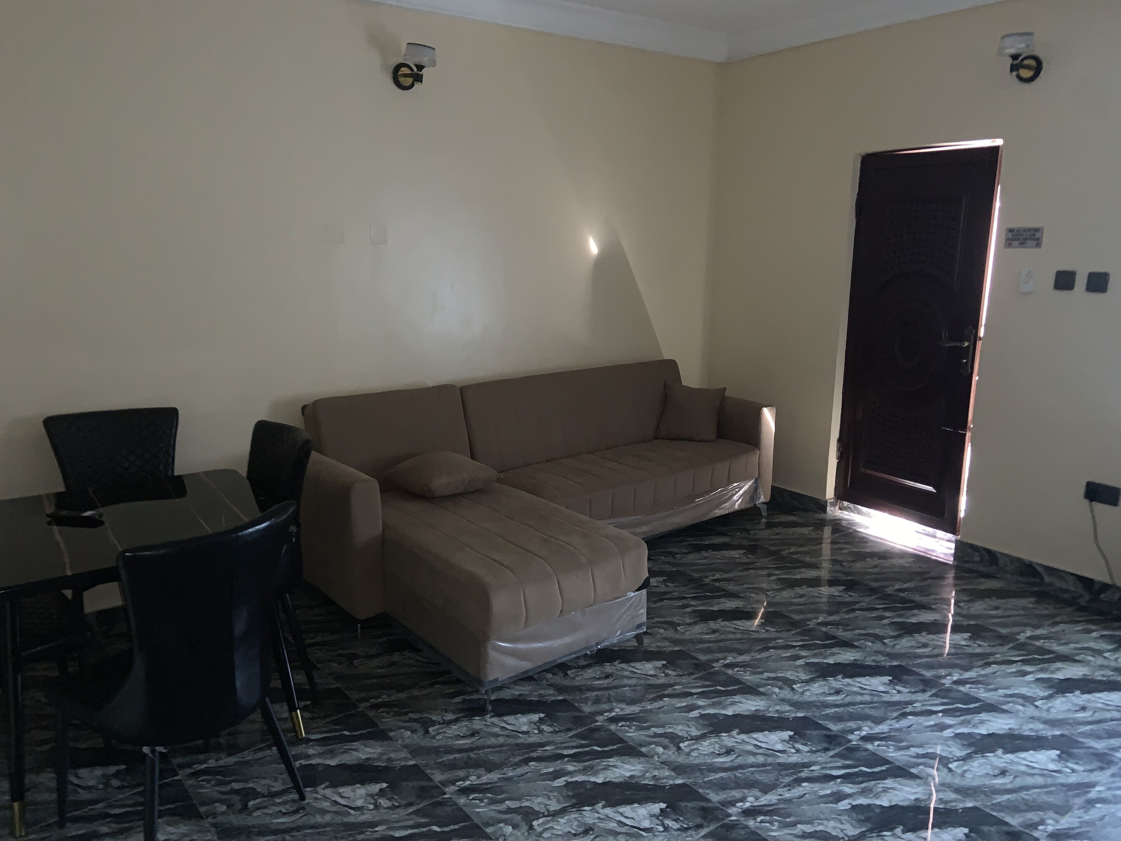 A room with a beige sofa, a small table, and two chairs. The floor has a marble pattern.