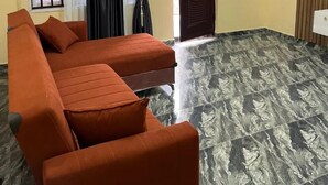 A room with a sofa, a door, a window with curtains, and a patterned floor. - Blue Icon Apartment  (Loburo)