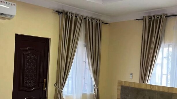 A hotel room with a bed, curtains, a wooden door, and a ceiling light. - Blue Icon Apartment  (Loburo)